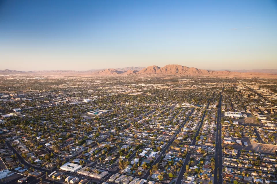 Aerial view of sprawling Las Vegas suburbs at golden hour with desert mountain in background.